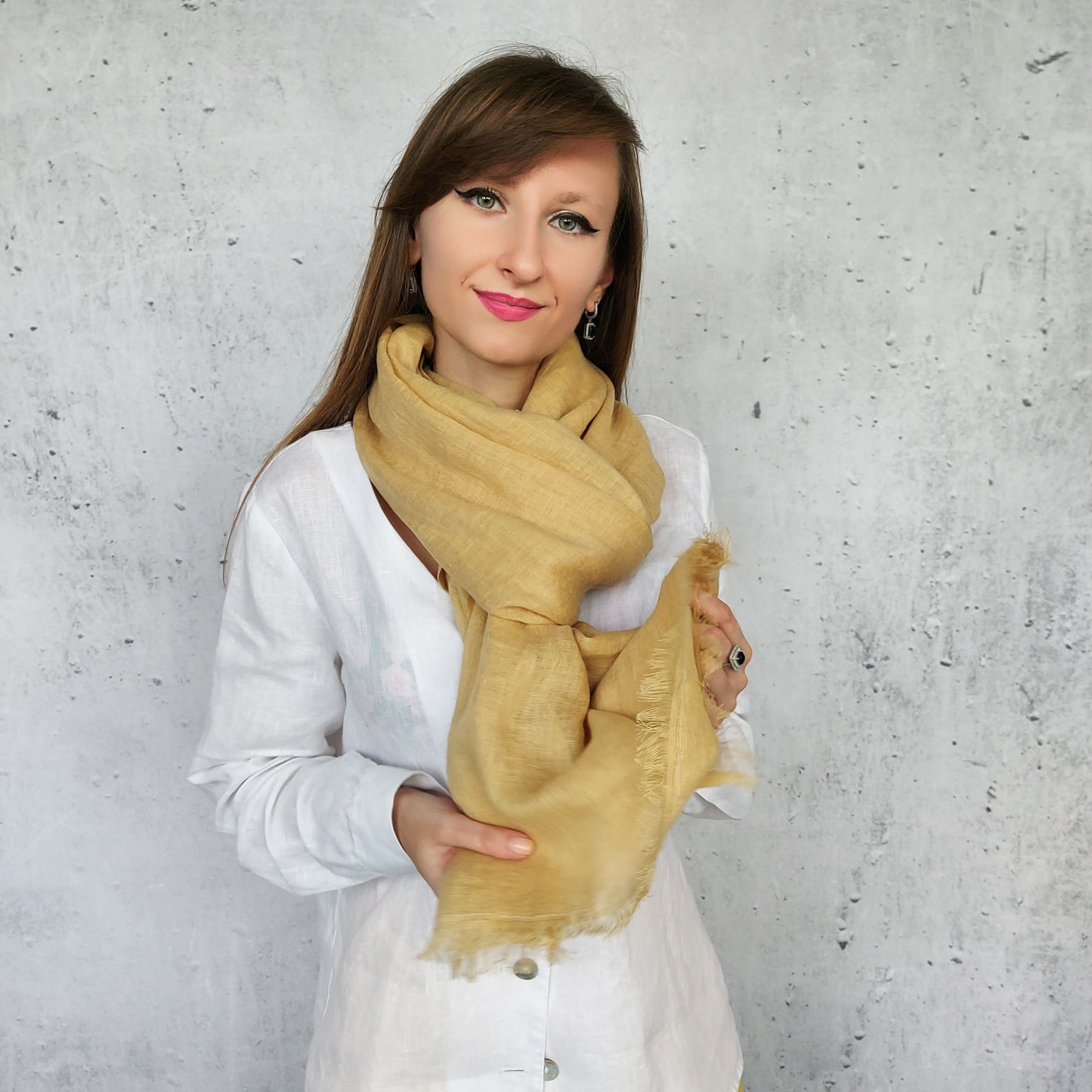 Woman wearing a beige sand scarf against a gray concrete wall