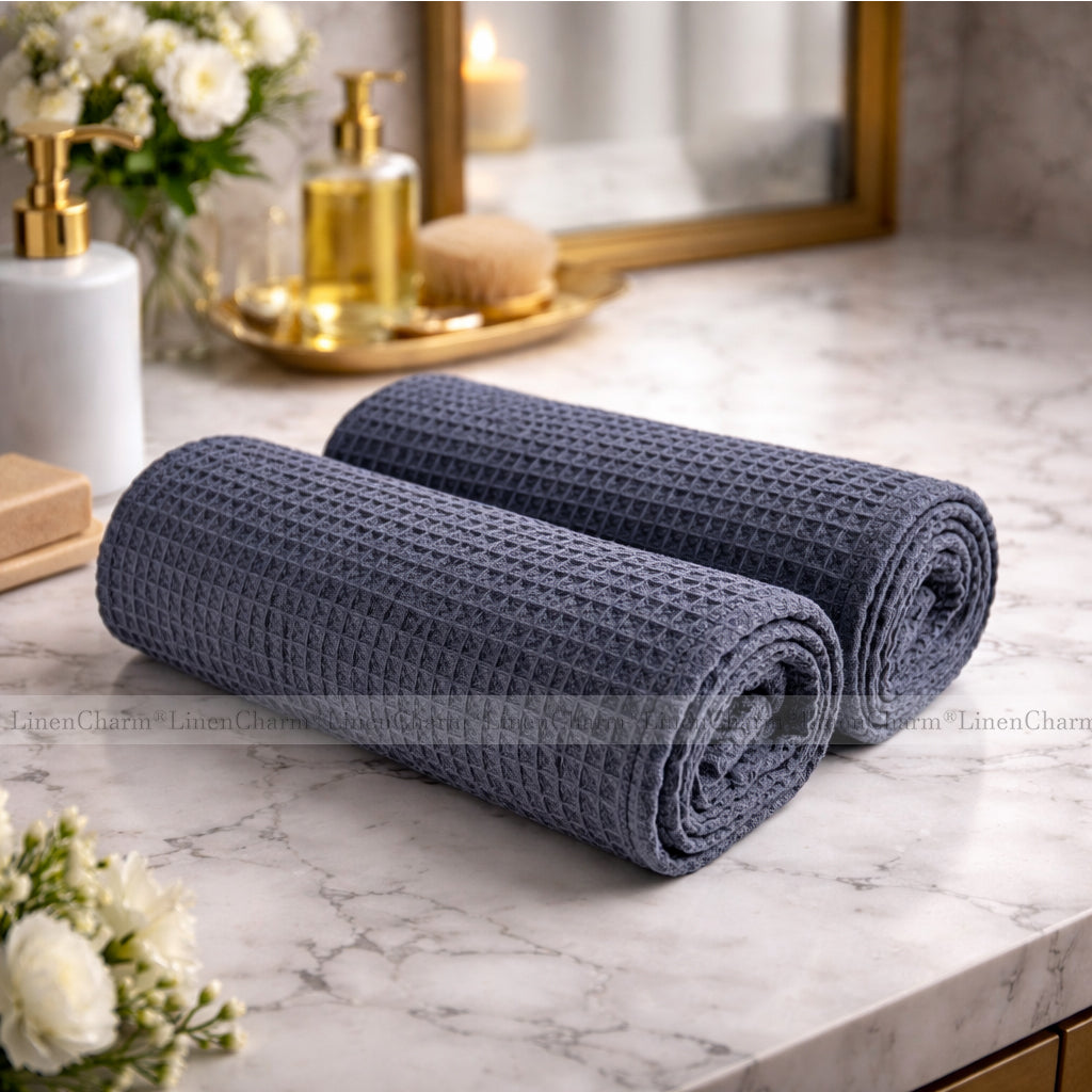 Two rolled-up anthracite towels on a marble countertop with decorative items in the background.