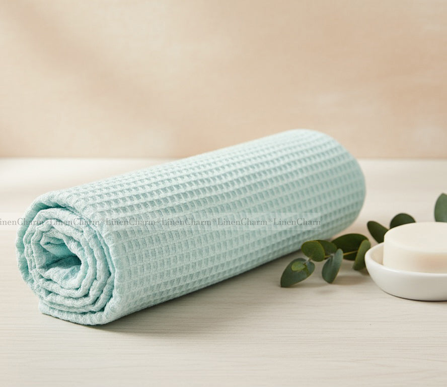 Rolled-up light mint towel on a beige surface with green leaves and a white bowl.