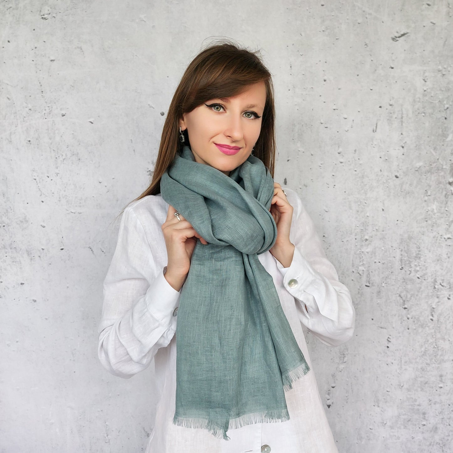 Woman wearing a dark mint scarf against a gray concrete wall