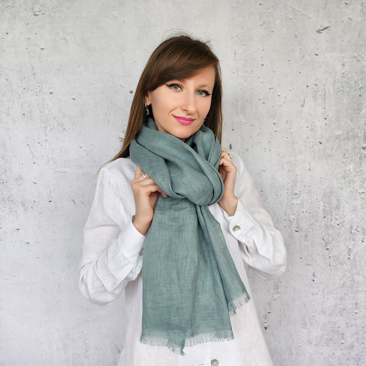 Woman wearing a dark mint scarf against a gray concrete wall