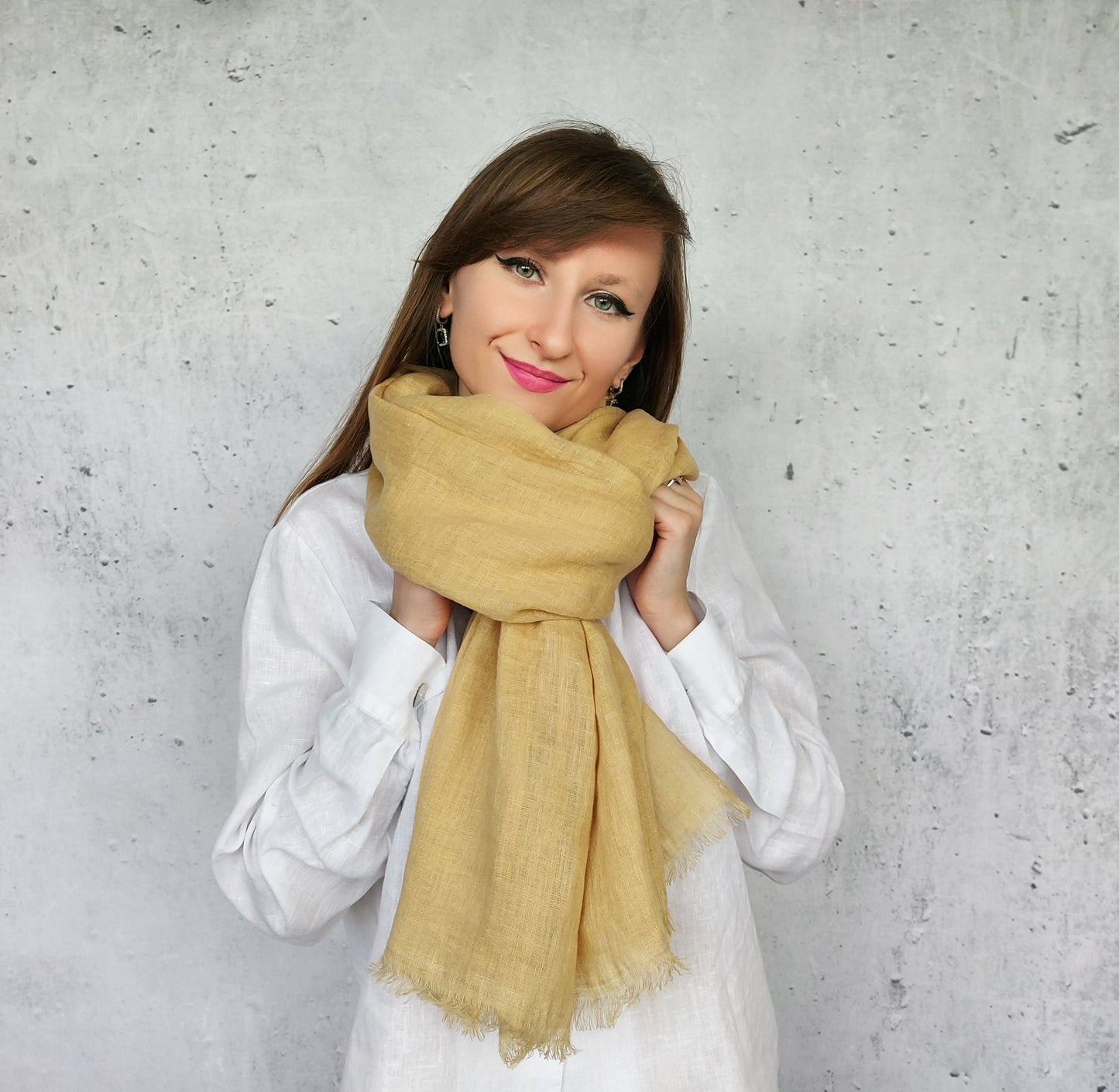 Woman wearing a beige sand scarf against a gray concrete wall