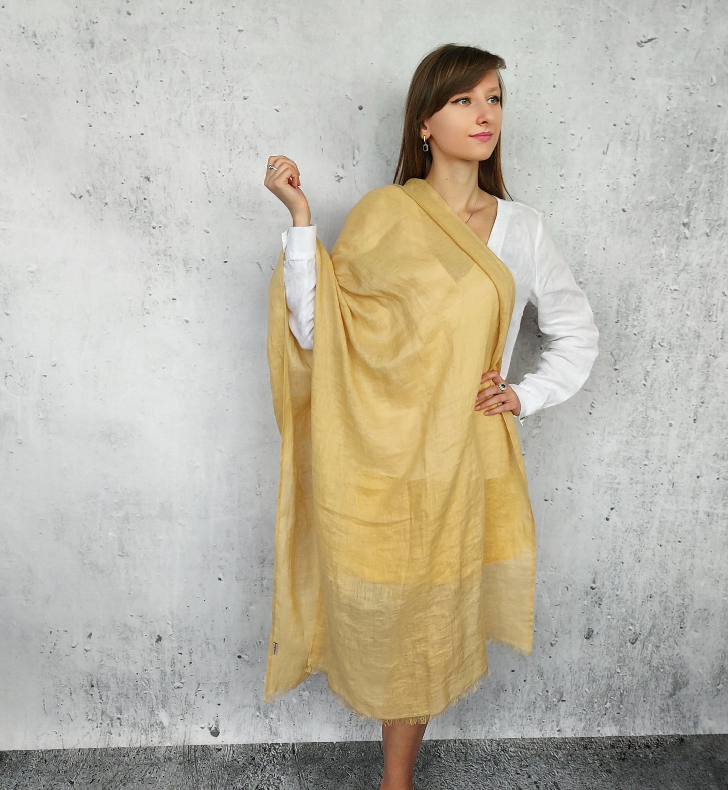Woman wearing a linen beige sand scarf against a gray concrete wall