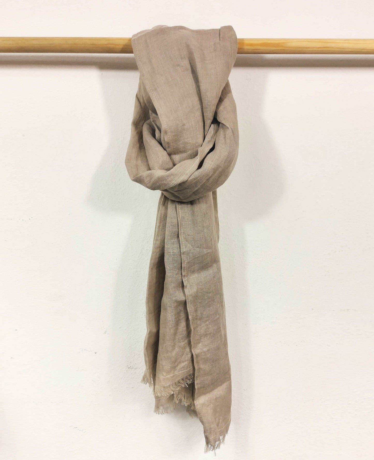 Natural scarf draped over a wooden rod on a white background