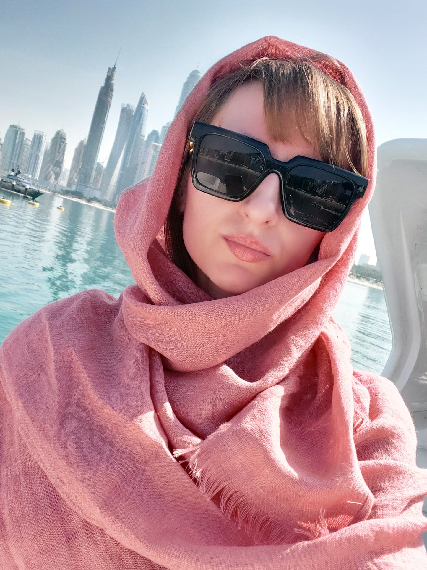 Person wearing a pink scarf and sunglasses with a city skyline and water in the background