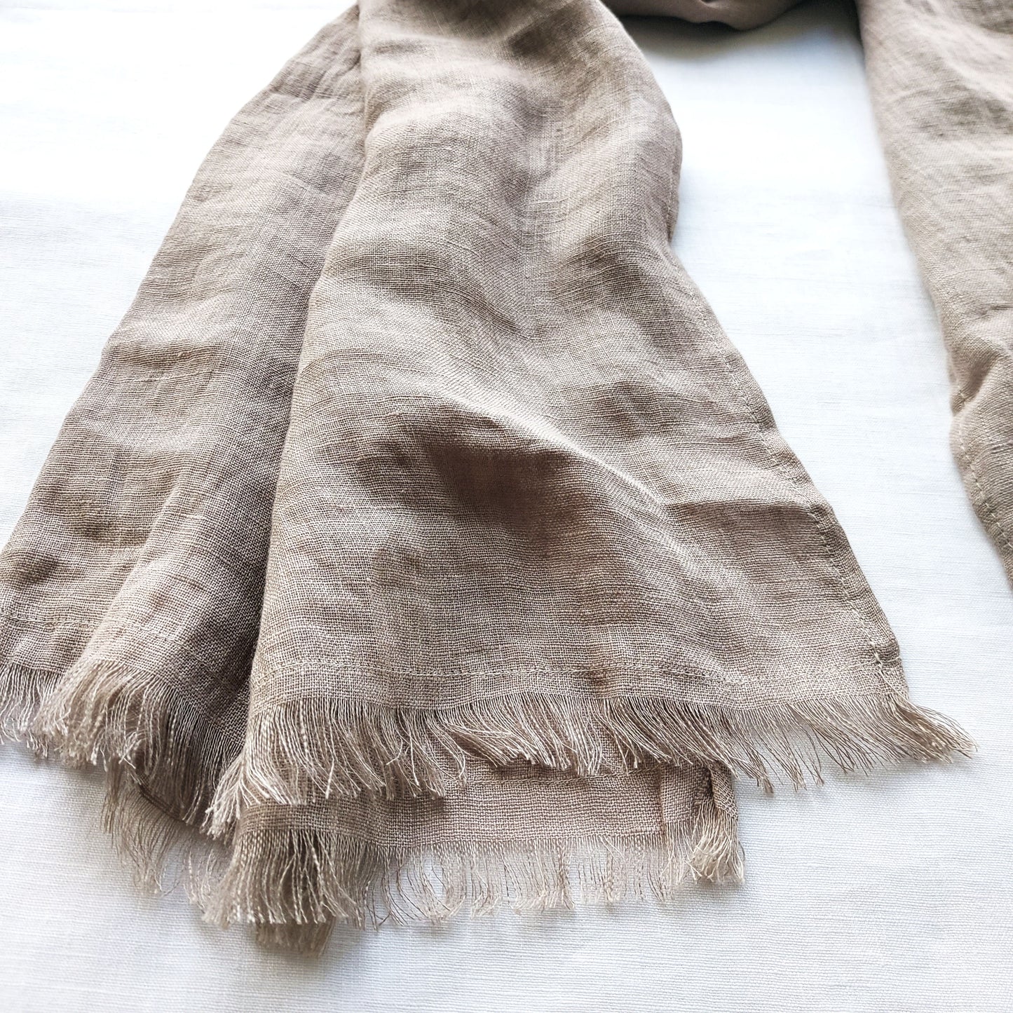 Linen natural scarf with frayed edges on a white surface