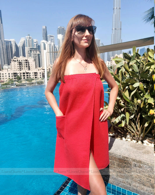 Woman in a red towel wrap standing by a pool with a city skyline in the background