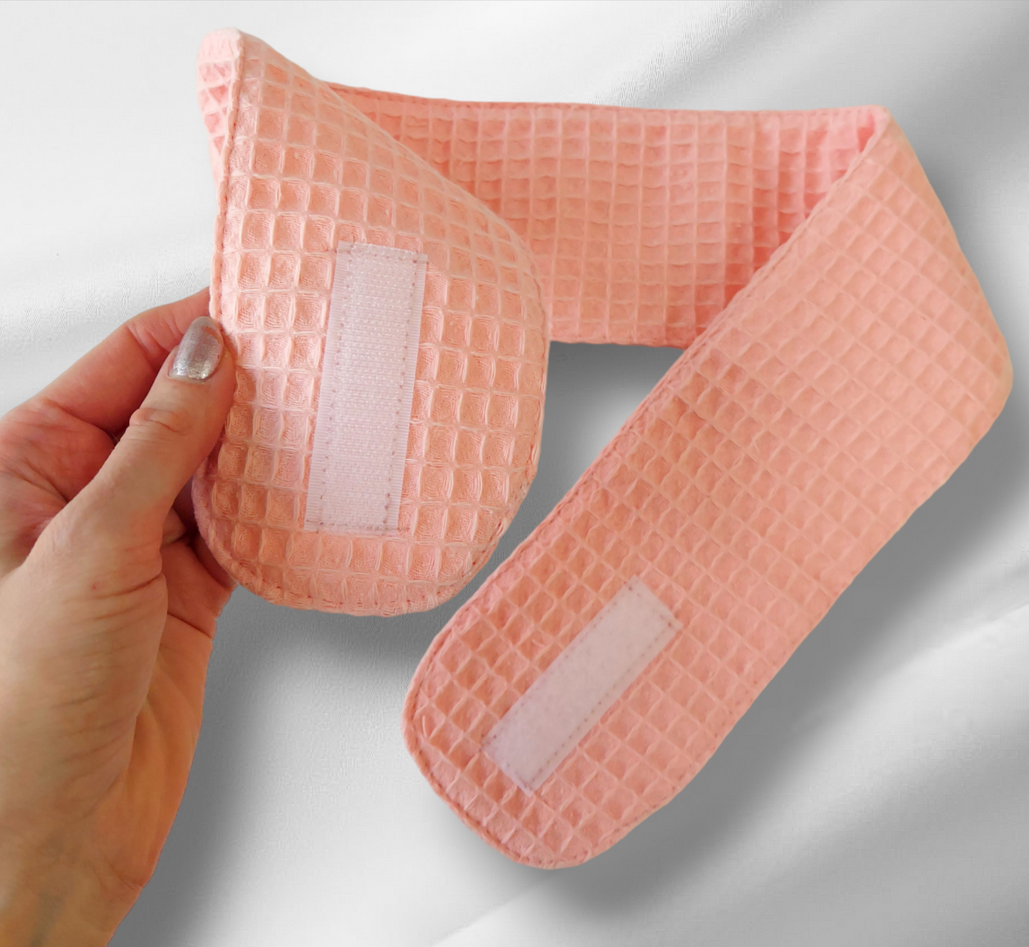 Pink textured belt with a hand holding it against a light gray background