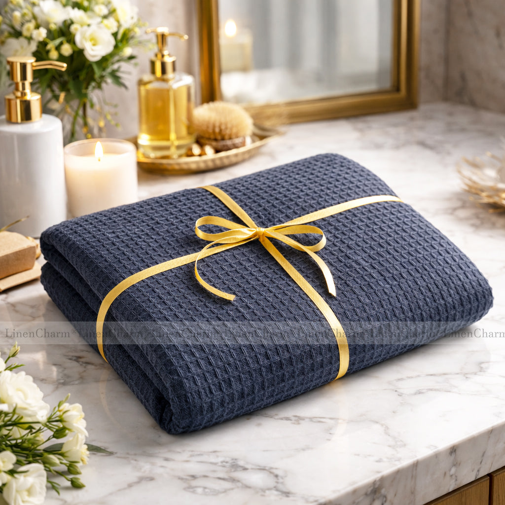 Folded anthracite towel with a gold ribbon on a marble surface with decorative items.