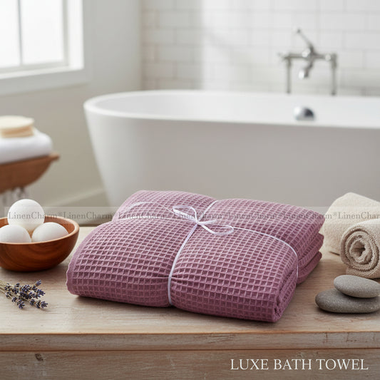 Pink waffle-textured bath towel on a wooden surface with a bathtub in the background.