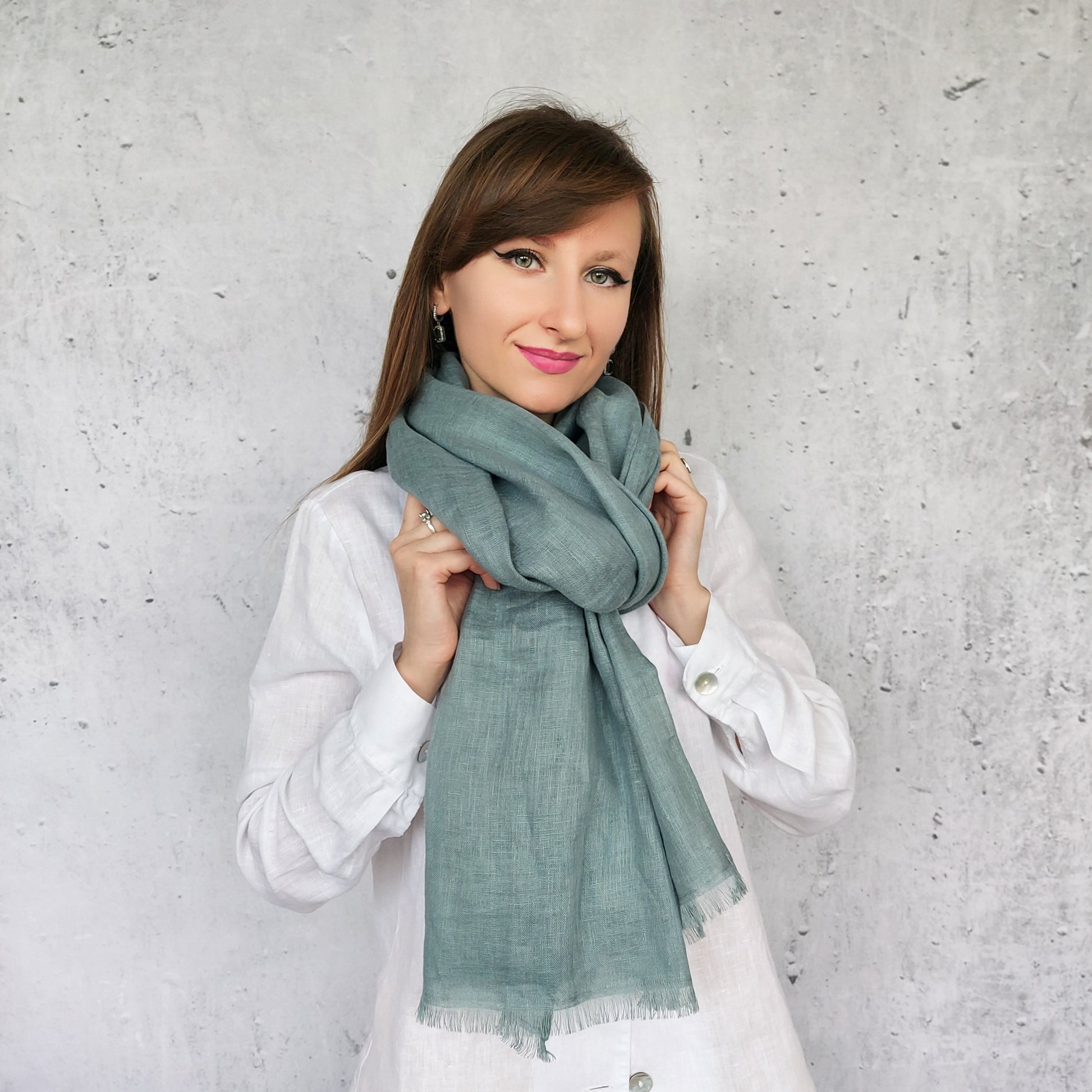 Woman wearing a dark mint scarf against a gray concrete wall