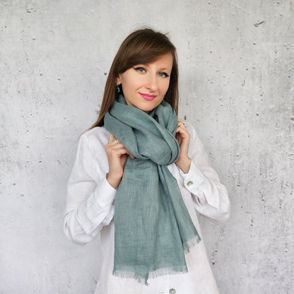 Woman wearing a dark mint scarf against a gray concrete wall