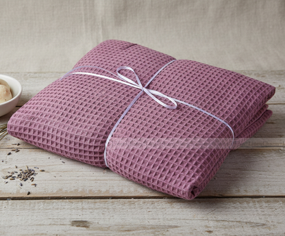 Folded pink textured blanket tied with a white ribbon on a wooden surface.