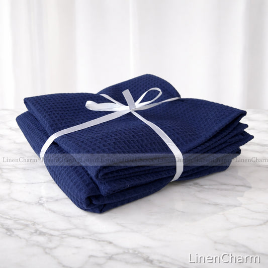 Folded navy blue blanket with a white ribbon on a marble surface, branded 'LinenCharm'.