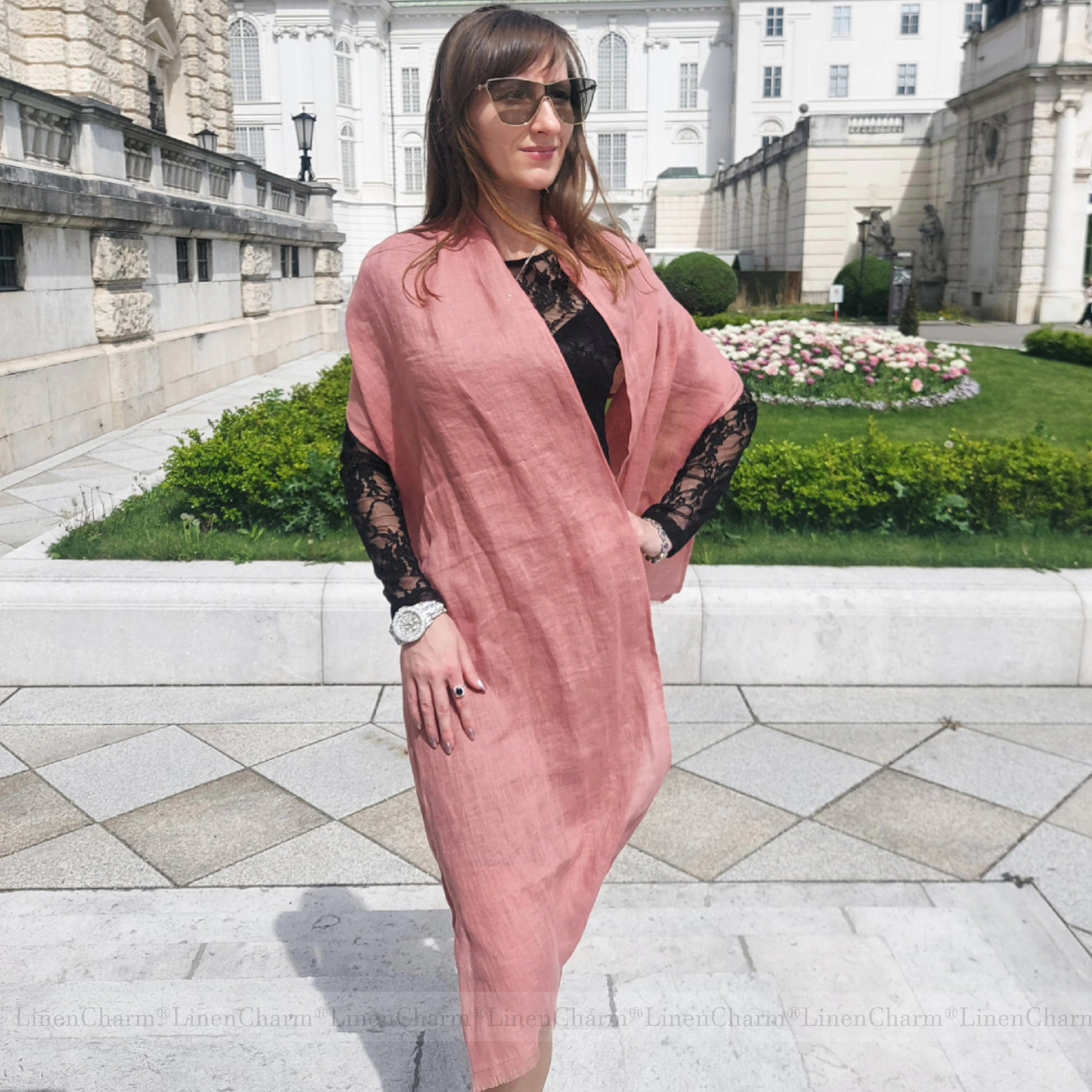 Woman in a salmon pink scarf standing in front of a historic building with gardens.