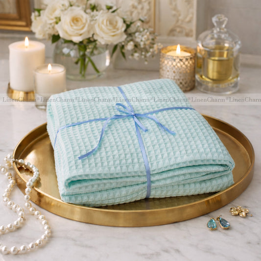 Folded light blue towel with a blue ribbon on a gold tray, surrounded by candles and flowers.
