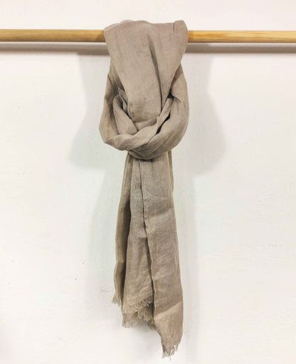 Natural scarf draped over a wooden rod on a white background
