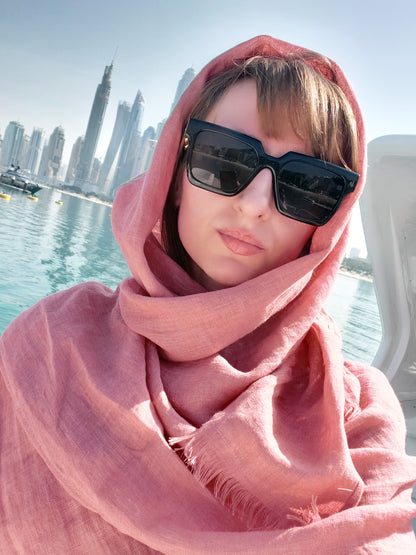 Person wearing a pink scarf and sunglasses with a city skyline and water in the background