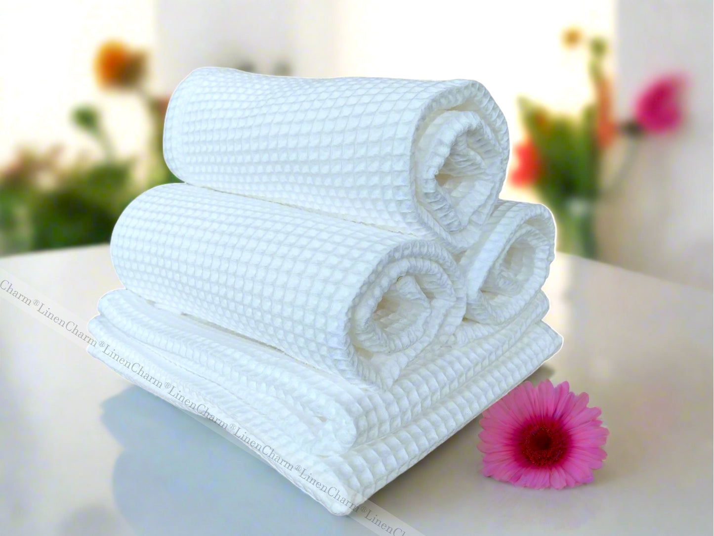 Stack of white towels on a light surface with a pink flower in the background