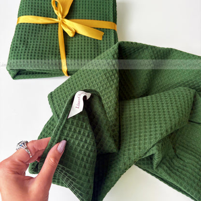 Green textured towel with a yellow ribbon and a hand holding it on a white background