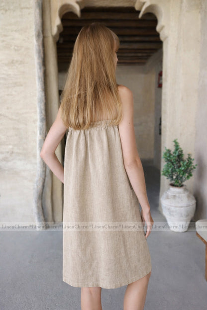 Woman wearing a beige dress standing in a stone-walled room with a plant in the background